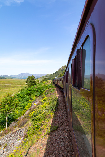 An image taken from the Jacobite Express, capturing the breathtaking views of the Scottish Highlands as seen from the train. The journey offers a unique perspective of Scotland's dramatic landscapes, with rolling hills, serene lochs, and rugged countryside unfolding outside the windows, embodying the romance and adventure of rail travel.