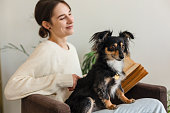 Young adult woman relaxing with a book and dog in living room