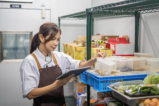 female restaurant worker checking stocks in freezer room in restaurant using digital tablet