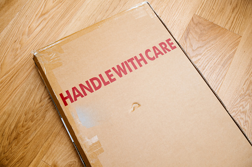 Handle with care inscription on the cardboard box of a new parcel delivered by freight transportation service - arranged on the wooden parquet floor