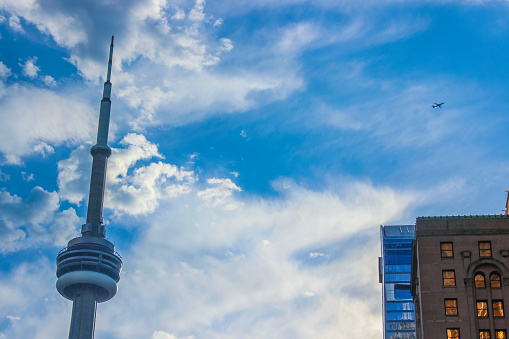 September 2023- Toronto, Canada: View on the Canadian National - CN - Tower (communications tower), taken from downtown Toronto by Union Station, with beautiful skies shortly after rain and the beginning of sunset and an airplane flying over.