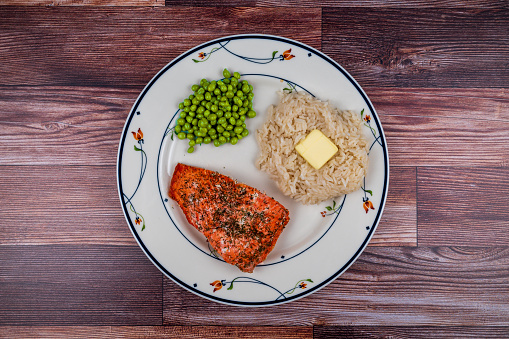Baked salmon fillet with Jasmine rice and peas isolated on wood background. Salmon is cooked with dill and rice has butter patty on it