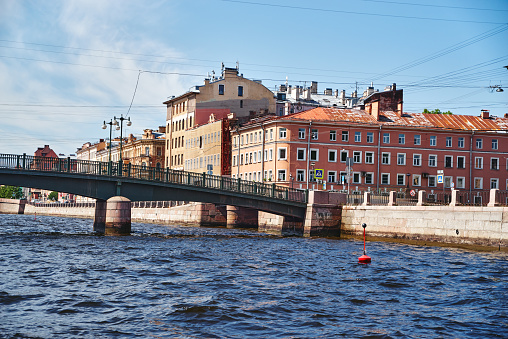 Cityscape of the embankment Fontanka river with bridge in sunny day, street and old residential buildings in the historical center of St. Petersburg, Russia, blue sky and water