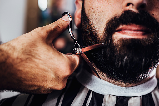Barber cutting a client's beard with a scissor. Beard cut in the barber shop.