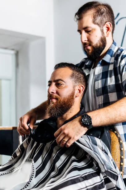istock Client of a barber shop getting hairdressing coat on his torso. 2006243649