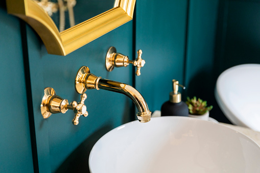 Retro-style brass faucet and a white sink against the emerald green wall.
