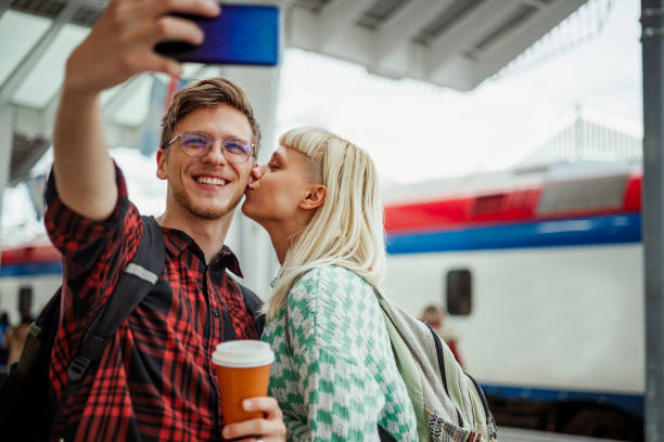 Couple at the train station waiting for their train while taking a selfie