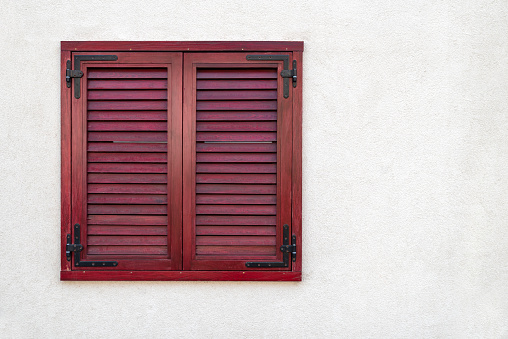 Red shuttered window on white stucco wall with copy space