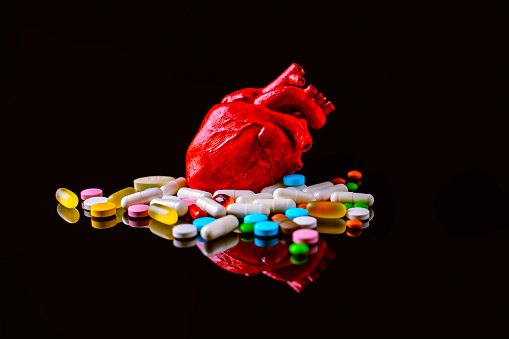 Concept of heart model surrounded by various pills on dark background