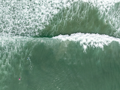 A high perspective of surf breaking with surfers sitting out past the shore break, great copy space.