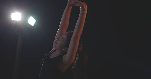Selective focus, Young female runner in sportswear listening to music with headphones while stretching after a workout in the outdoor sports stadium at night time.preparing for evening workout.healthy lifestyle.