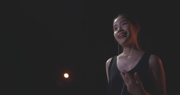 Low angle view, Young female runner in sportswear listening to music with headphones while stretching before a workout in the outdoor sports stadium at night time.preparing for evening workout.healthy lifestyle.