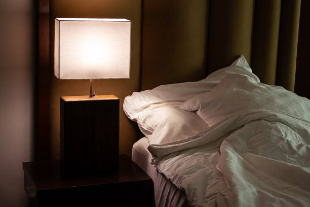 Pillows, bed and lamp light on table in hotel for travel, accommodation or holiday rental. Interior, furniture and rustic bedroom at vacation home with comfortable sheets, cushions and headboard.