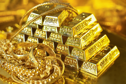 Gold bars and gold jewelry on the golden reflect light background. Gold is hard commodity good, risk asset, tangible value that used to be gold reserve, fund reserve,