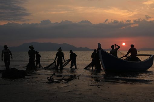 Banda Aceh 03/25/2019 , The reddening dusk beautifies the sky in Kampung Jawa, Banda Aceh, illuminating the fishermen as they diligently clean their fishing nets. The sunset reflects off the colorful sea, creating a stunning and soothing sight after a day of hard work at sea.