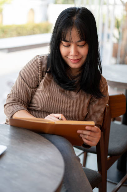 istock A positive Asian female is keeping her diary or listing her ideas in a book while sitting in a cafe. 2006647152