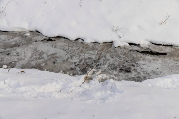 a narrow small river in winter covered with snow and ice, the ice on the river is reinforced with a plastic geogrid