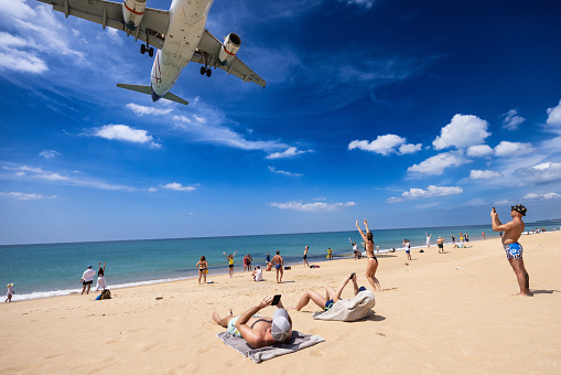 Tourists take selfies and pose for pictures under the low flying jets landing at Phuket International airport
