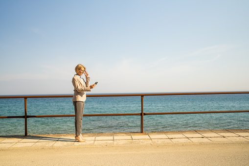 Female real estate agent talking on mobile phone while walking by the sea