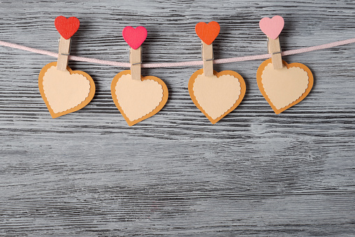 Four heart-shaped paper cutouts clipped to a pink string against a rustic wooden background. Perfect for Valentine's Day or love-themed events