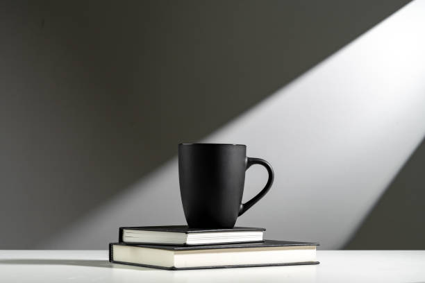 Black cup on books in sunlight on gray background close up