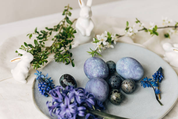 stylish easter eggs on vintage plate, bunny and spring flowers on rustic table. happy easter! natural dye blue eggs, purple hiacynt blossoms on linen napkin. holiday setting, minimal still life - easter egg figurine easter holiday стоковые фото и изображения