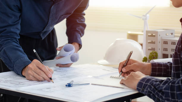 istock Engineers are helping to design work on blueprints with wind turbine model. Eco-friendly building. Corporate building reduce CO2. Sustainable development environmental. Construction and structure. 2006990452