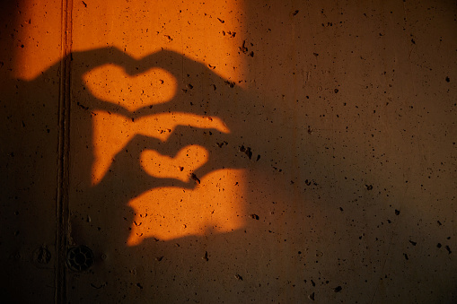 Shadow on the wall of unrecognizable people making heart shapes with their hands. Copy space.