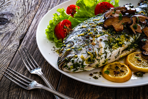 Baked sea bream, mushrooms and fresh vegetables on wooden table