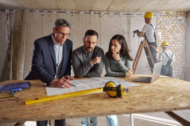 istock Young couple and their agent examining blueprints at construction site. 2007030603