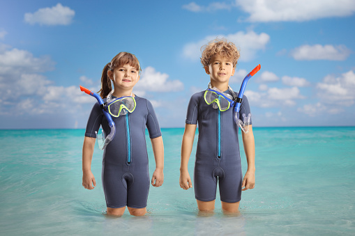 Girl and boy in wetsuits and diving masks standing in the sea