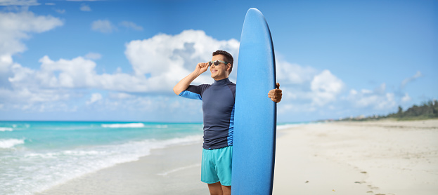 Man with sunglasses and a surfing board standing on a beach in Cuba, Varadero