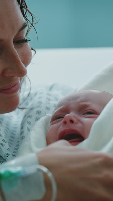 Mother looking at infant crying on bed in hospital