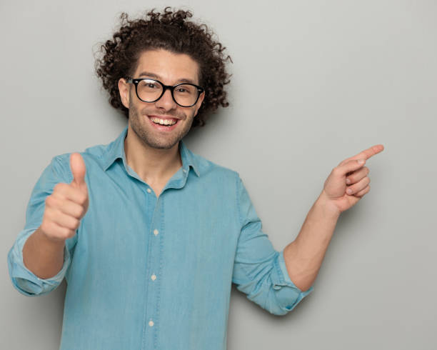 istock handsome casual man with glasses pointing finger to side and making thumbs up gesture 2007130112