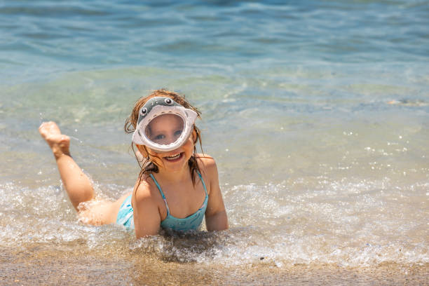 Happy little girl wearing shark swim mask posing in the shallow waves of a sunny beach