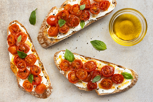 Tomato and cream cheese bruschetta with basil and olive oil, on stone background