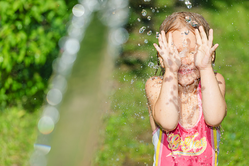 Happy little girl wearing swimsuit enjoying palying with a garden hose jet on a hot summer day