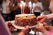 Hands of young people holding a happy birthday cake with their friends Candle flame lights on birthday cake during celebration