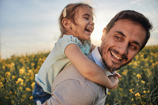 Young father and daughter in field on a sunset. Single father is carrying little girl.