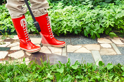 Person in red gumboots power washing garden path