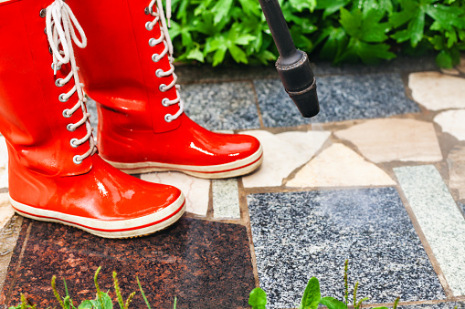 Person in red gumboots power washing garden path