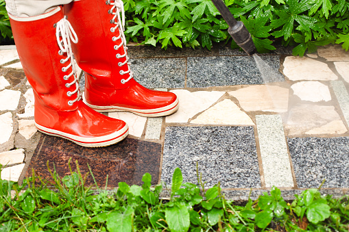 Person in red gumboots power washing garden path