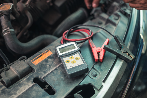 A digital battery tester connected to a car battery, checking for performance and charge level.