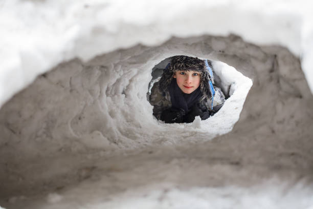 A teenage boy is lying on his back on fresh snow, sprinkled with white flakes. His glasses are covered in snow, as well as his hat and scarf.Shot with Canon R5