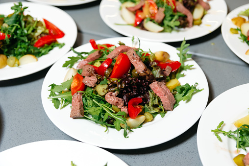 A healthy beef salad with arugula, red peppers, and mixed greens, served on a white plate, ideal for a nutritious meal.