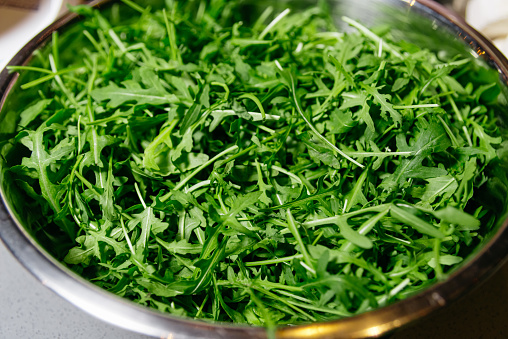 A stainless steel bowl full of green, fresh arugula leaves, ready to be used in healthy salads and dishes.