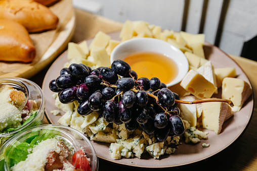 A variety of gourmet cheeses accompanied by fresh black grapes and a bowl of honey, perfect for a cheese board setup or a wine pairing event.