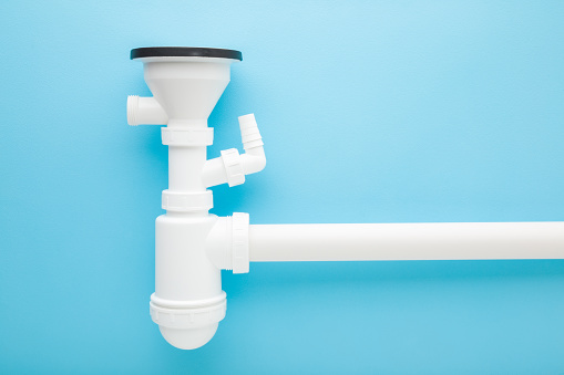Assembled white new plastic parts for sink drain siphon on light blue table background. Pastel color. Closeup. Top down view.