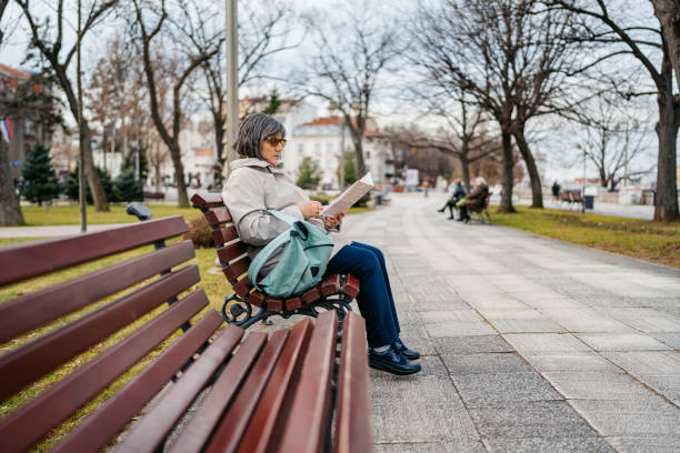 Beautiful senior woman reading a map while sitting on the bench in the park in autumn.