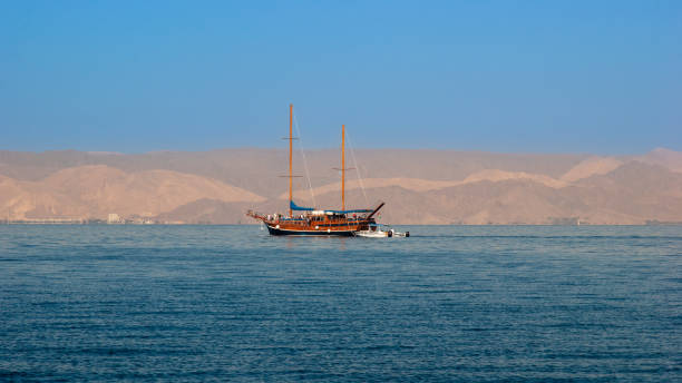 giordania. aqaba. "hotel movenpick resort e spa tala bay aqaba 5 stelle" sul mar rosso. yacht a due alberi in mare sullo sfondo della costa montuosa di israele. - backdrop old fashioned outdoors yacht foto e immagini stock